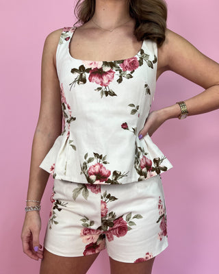 Woman wearing a floral peplum top and shorts set against a pink background