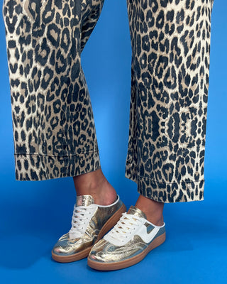 Leopard print pants with gold and white sneakers on a blue background