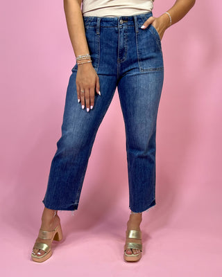 Person wearing blue jeans and gold sandals on a pink background