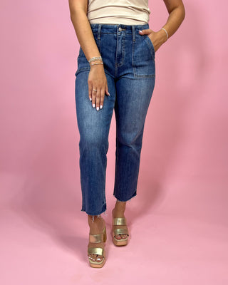Person wearing blue jeans and gold sandals on a pink background