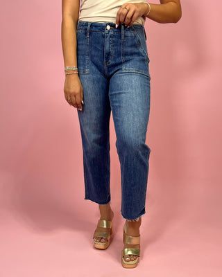 Person wearing blue jeans and gold sandals on a pink background