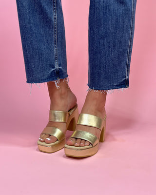Gold platform sandals worn with blue jeans on a pink background