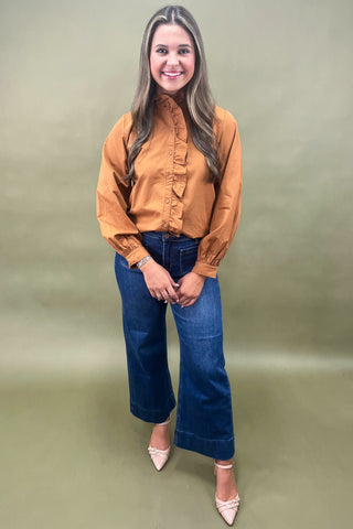 Woman wearing a mustard yellow blouse and blue jeans against a green background