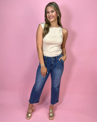 Woman wearing a white sleeveless top and blue jeans against a pink background