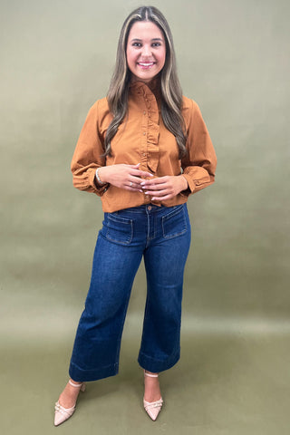 Woman wearing a brown blouse and blue jeans against a green background