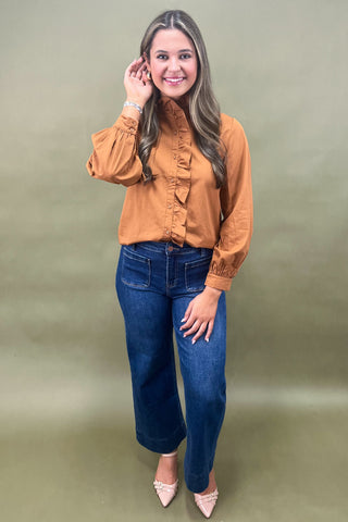 Woman wearing a mustard yellow blouse and blue jeans against a green background
