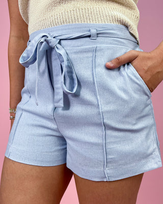 Light blue shorts with a tie waist worn by a person on a pink background