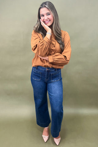 Woman wearing an orange blouse and blue jeans against a green background