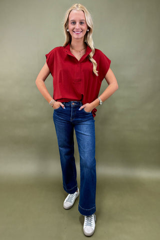 Woman wearing a red blouse and blue jeans against a plain background