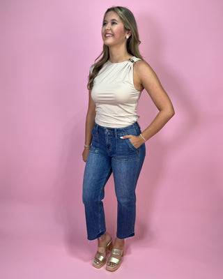 Woman wearing a white top and blue jeans against a pink background