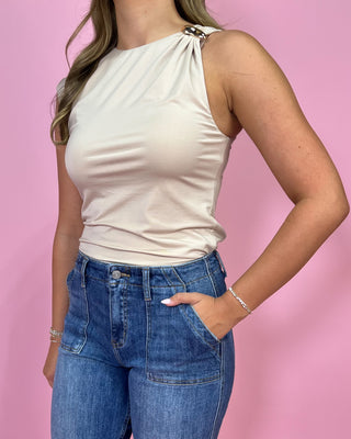 Woman wearing a beige sleeveless top and blue jeans against a pink background