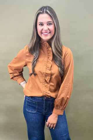 Woman wearing a mustard yellow blouse and blue jeans against a green background