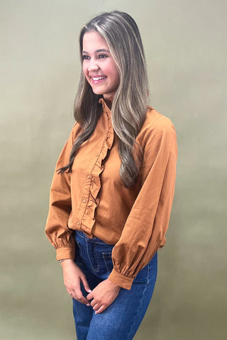 Woman wearing a brown blouse and blue jeans against a plain background