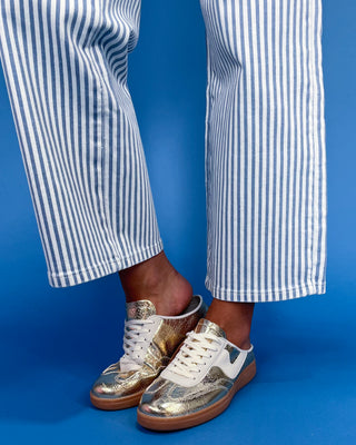 Gold and white sneakers worn with blue and white striped pants against a blue background