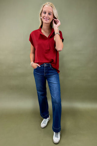 Woman wearing a red blouse and blue jeans against a green background