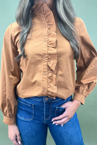 Person wearing a brown button-up shirt and blue jeans against a light green background