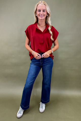 Woman wearing a red blouse and blue jeans against a beige background