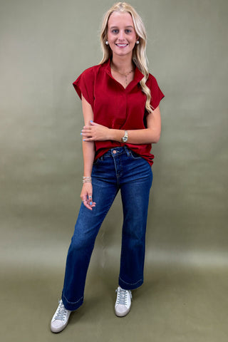 Woman wearing a red shirt and blue jeans against a plain background