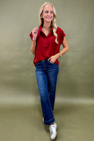 Woman wearing a red blouse and blue jeans against a green background
