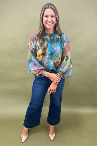 Woman wearing a colorful patterned blouse and blue jeans against a green background
