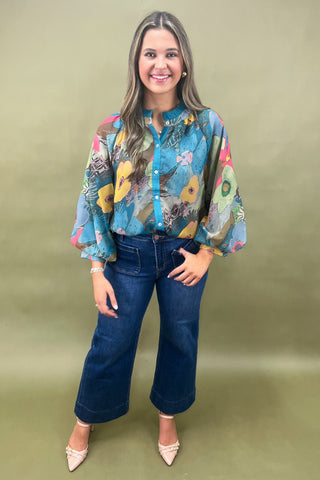 Woman wearing a colorful floral blouse and blue jeans on a green background