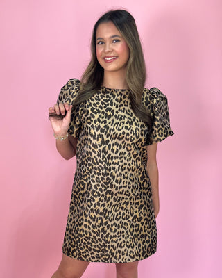 faux Leopard print mini dress with short flutter sleeves, a round neckline, and a relaxed shift silhouette, styled with gold strappy heels against a pink background.