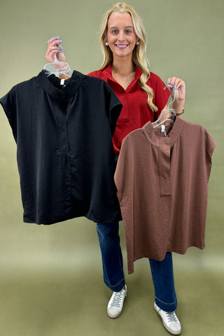 Woman holding two shirts, one black and one brown, against a plain background