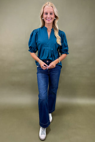 Woman wearing a blue blouse and jeans against a beige background
