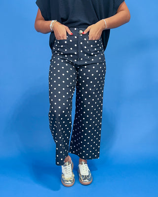 Person wearing navy blue pants with white polka dots against a blue background