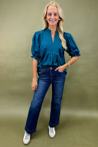 Woman wearing a teal blouse and blue jeans against a green background