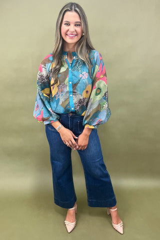 Woman wearing a colorful patterned blouse and blue jeans on a green background