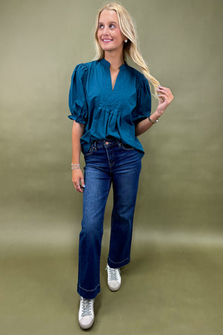 Woman wearing a teal blouse and blue jeans against a green background