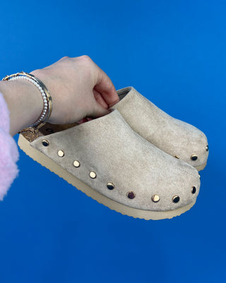 Nude suede-look slip-on clog mules featuring metallic round studs, closed rounded toes, and cork-look footbeds.