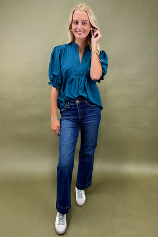 Woman wearing a teal blouse and blue jeans on a beige background