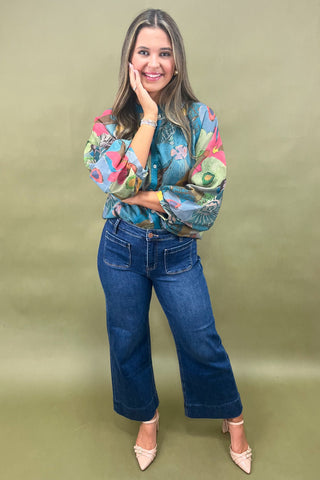 Woman wearing a colorful blouse and blue jeans against a green background
