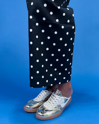 Person wearing black pants with white polka dots and gold sneakers on a blue background
