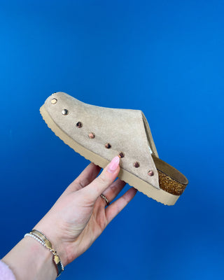 Nude suede-look slip-on clog mules featuring metallic round studs, closed rounded toes, and cork-look footbeds.