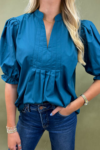Woman wearing a blue blouse with puffed sleeves against a green background