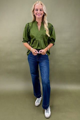 Woman wearing a green blouse and blue jeans against a green background