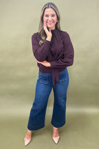 Woman wearing a maroon sweater and blue jeans against a green background