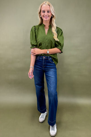 Woman wearing a green blouse and blue jeans against a plain background