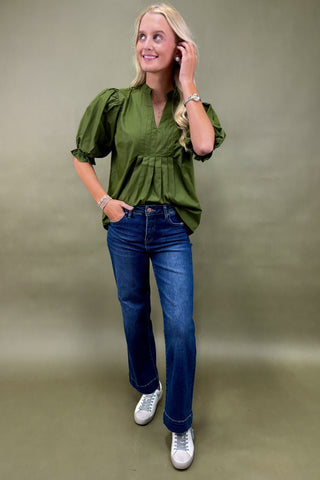 Woman wearing a green blouse and blue jeans against a plain background