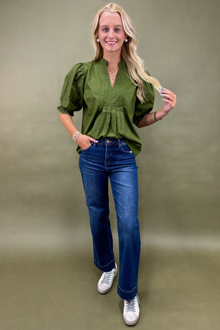 Woman wearing a green blouse and blue jeans against a green background