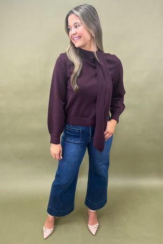 Woman wearing a purple sweater and blue jeans against a green background