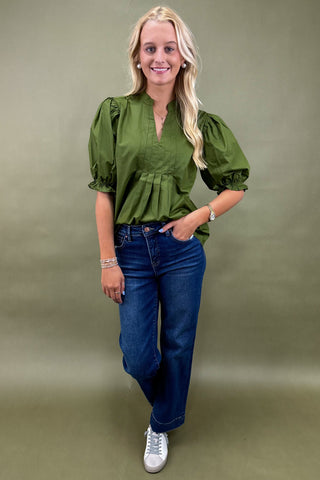 Woman wearing a green blouse and blue jeans against a green background