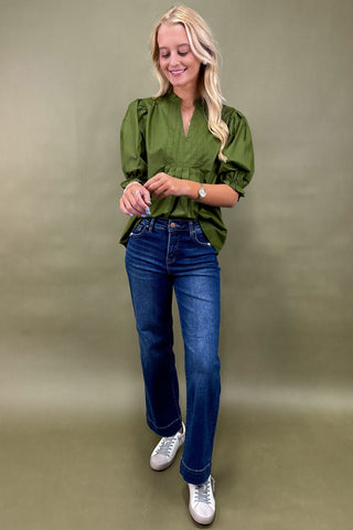 Woman wearing a green blouse and blue jeans against a plain background