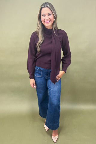 Woman wearing a dark purple sweater and blue jeans against a green background