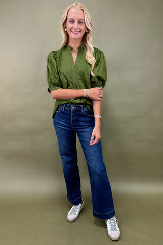 Woman wearing a green blouse and blue jeans against a beige background