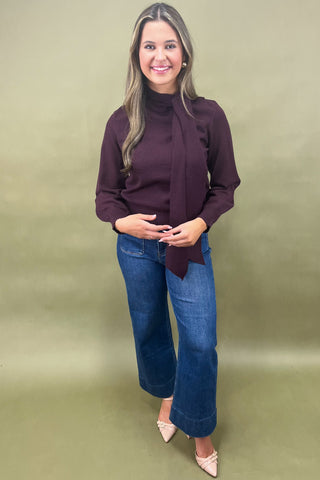 Woman wearing a purple sweater and blue jeans against a green background