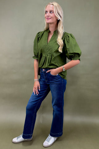 Woman wearing a green blouse and blue jeans against a beige background